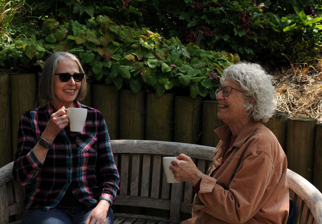 Two members of the group sitting on a bench and enjoying a cup of tea and a chat in the sunshine.