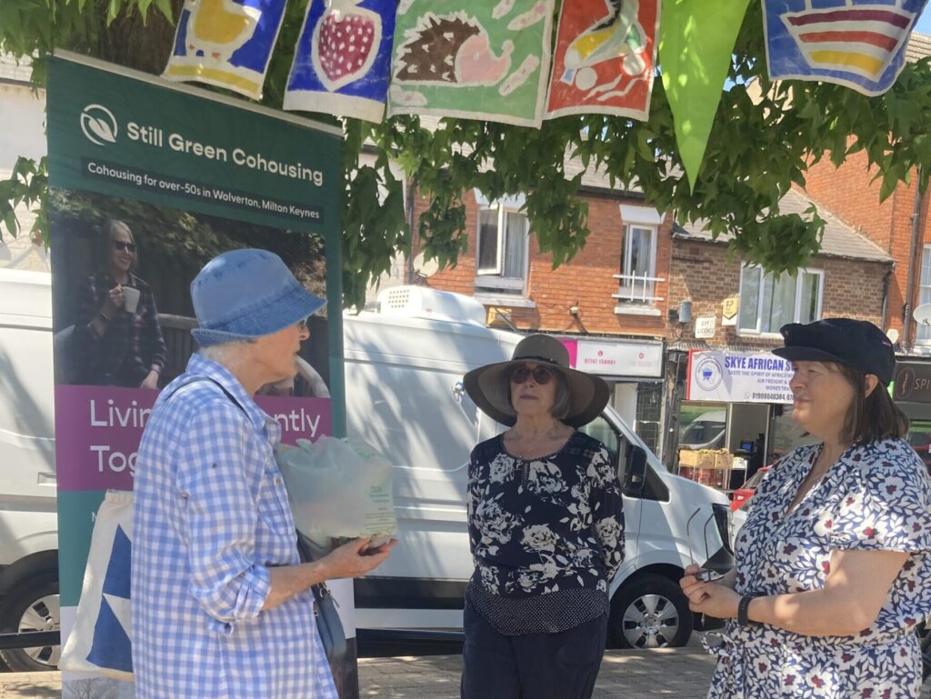 3 members of Still Green at a stall at Wolverton Market in dappled shade under a tree